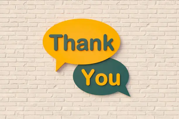 Photo of Thank you. Sign, speech bubble, text in yellow and dark green against a brick wall.