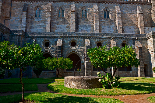 View across the lawn in the inner courtyard of Evora cathedral. Orange trees and well in the quadrangle with the cloisters in the background.