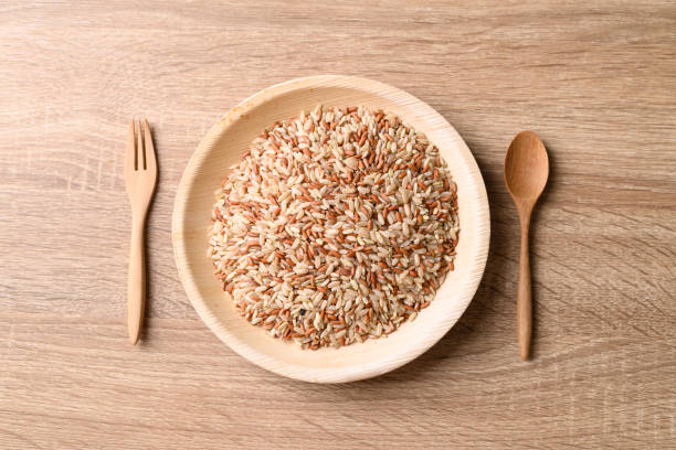 Organic brown Thai rice grain in natural plate with spoon and fork on wooden background, Table top view