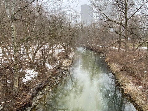 Stream flowing through a city park on a cold winter day with snow falling