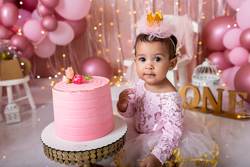 Adorable little girl smashing the cake during her first birthday party with ballons