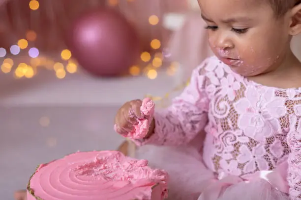 Adorable little girl smashing the cake during her first birthday party with ballons