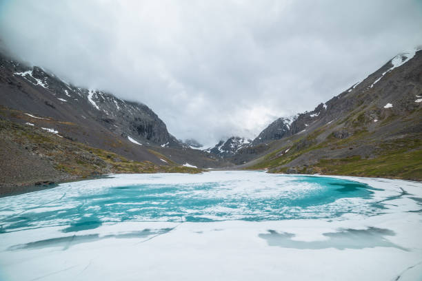 istock Atmospheric mountain landscape with frozen alpine lake and high snowy mountains. Awesome overcast scenery with icy mountain lake on background of snow mountains in low clouds. Scenic view to ice lake. 1387745828