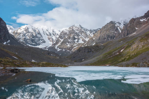 istock Atmospheric landscape with frozen alpine lake and high snow mountains. Ice floats on transparent water surface of mountain lake. Awesome scenery with large snowy mountains reflection in clear lake. 1387745832