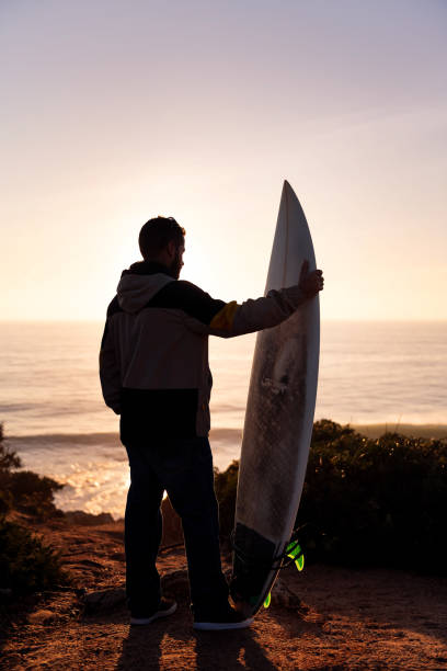 istock man looking at the sea at sunset with a surfboard 1387746084