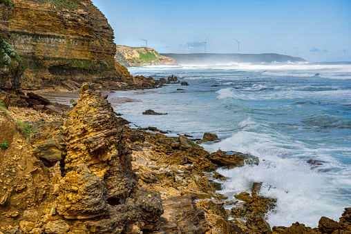 Waves crashing to shore at Yellow Rock with the wind turbines in the background on the cliffs