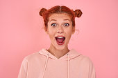 Emotional red-haired woman screaming in craziness with ecstatic overjoyed feeling on pink background