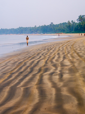 Sindhudurg, India - December  20, 2021 : Unidentified couple jogging at beach side during morning hours. Beautiful texture of sea sand. vertical or portrait orientation