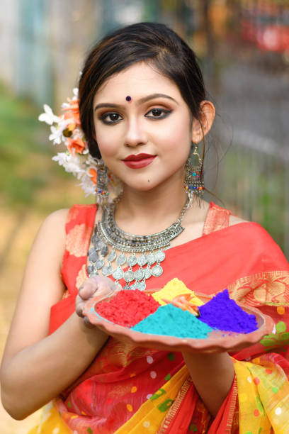 Portrait of pretty young indian girl wearing traditional saree and jewellery, holding powder colours in plate on the festival of colours called Holi, a popular hindu festival celebrated across India. stock photo