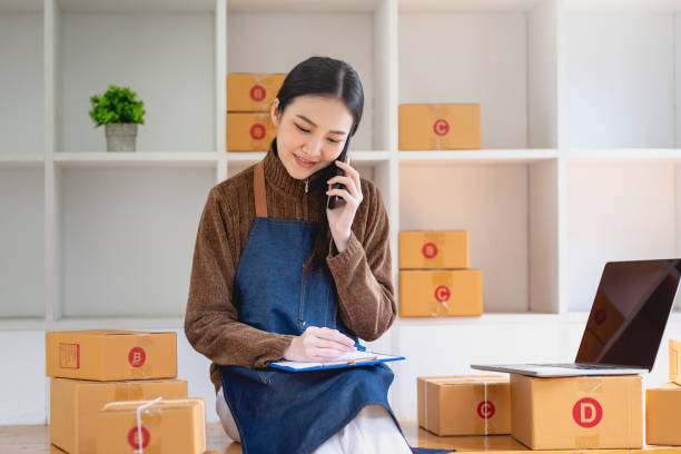 Online sales business owner woman talk on the phone and taking note of the customer's address prepared for delivery. stock photo
