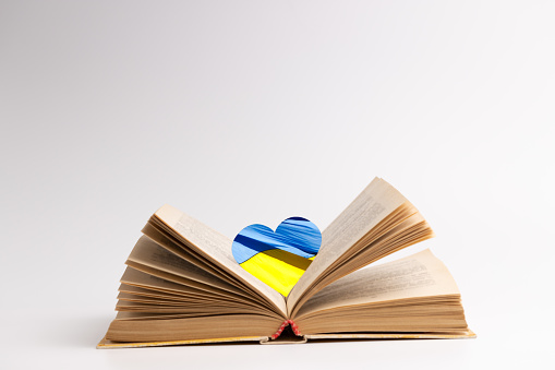 open book with heart symbol colored ukrainian flag over grey background. copy space. side view. concept.
