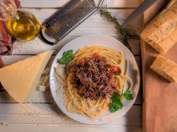 Bucatini Bolognese Pasta Dish with bread and cheese top view on white table stock photo