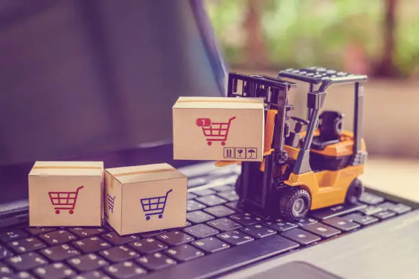Photo of Logistics and supply chain management for online shopping concept : Fork-lift moves a box with a red shopping cart logo, 2 cartons on a laptop computer.