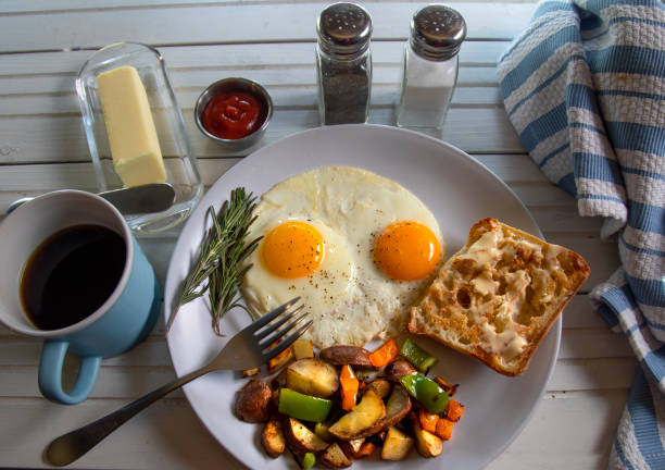 Fried eggs with hash browns and toast and butter on natural white wood table top view