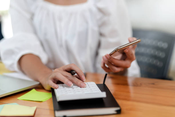 istock Close up. Woman hand using mobile phone and calculator working at office. 1387770566