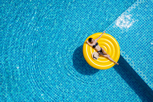 Top view of young asian woman in bikini on the yellow inflatable ring in the pool at private villa. Summer holiday concept