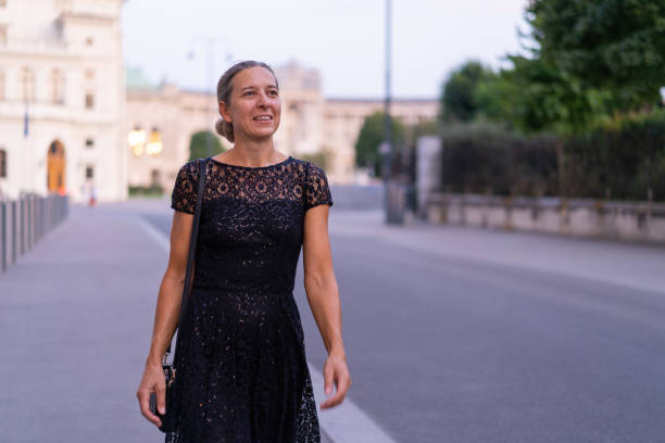 Woman in black dress walking through city of Vienna medium shot happy smiling mature adult woman in her forties in beautiful black cocktail dress walking alone through old town of european city going out, shallow focus, copy space cocktail dress stock pictures, royalty-free photos & images