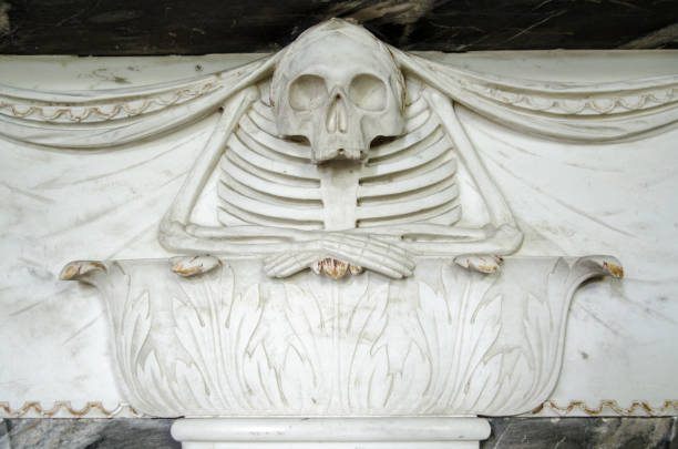 Carving of a skeleton resting on an acanthus plinth