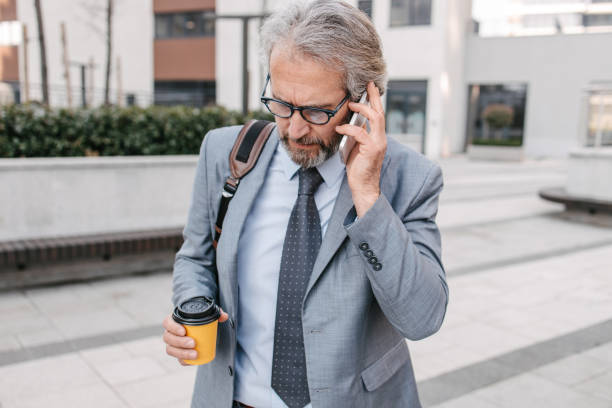 istock Businessman in a suit holding coffee to go and using smartphone 1387781105