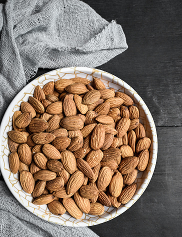 Almonds in white porcelain bowl on dark background. Almond concept with copyspace.