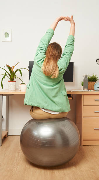 donna che si allunga mentre lavora da casa da remoto - yoga ball foto e immagini stock