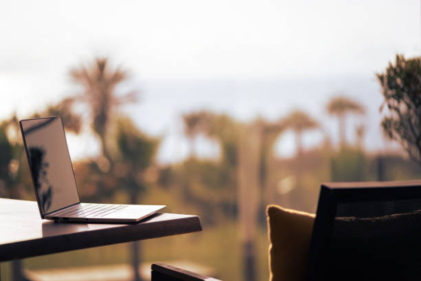 Laptop on table on balcony opposite sunset palm sea beach. Remote work on the vacation. Rear view stock photo