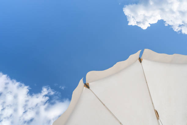 Bottom view on white beach or pool umbrella and blue sky with small cloudy. Copy space. Holiday, vacation, travel concept