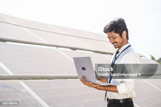 Smiling Engineer Checking Operation By Working On Laptop In Front Of Solar Panel At Farmland Concept Of Technology Sustainable Lifestyle And Professional Occupation Stock Photo - Download Image Now