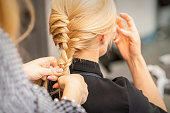 Braiding braid. Hands of female hairdresser braids long braid for a blonde woman in a hair salon.