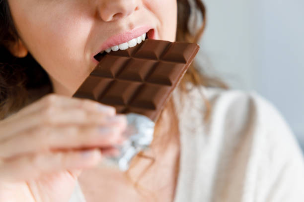 mujer mordiendo una barra de chocolate - chocolate fotografías e imágenes de stock