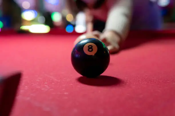 Pool ball on a red table with a person's arms from behind.
