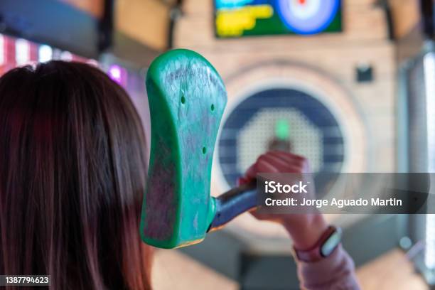 Rear View Of A Woman Holding An Axe For Recreational Throwing In An Arcade Stock Photo - Download Image Now
