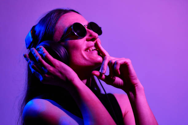 ネオンの背景にヘッドフォンで音楽を聴いているサングラスをかけたかわいい女性 - music women disco joy ストックフォトと画像