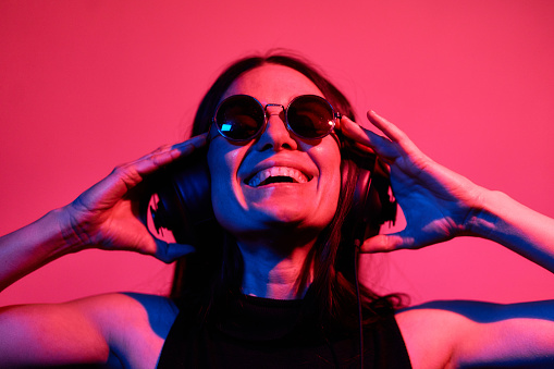 Pretty woman listening to music with headphones on neon lights background