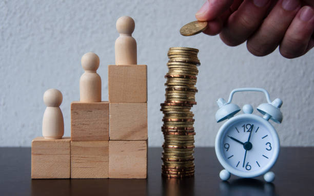 istock Coins Stack with wooden doll model, hand and alarm clock background - Business Concept 1387803239