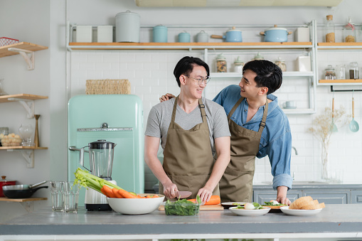 Young Asian LGBTQ gay couple preparing vegetables and food for cooking together at kitchen