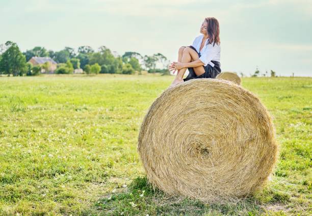 istock A beautiful young woman sitting on a haystack on a green field. 1387804664
