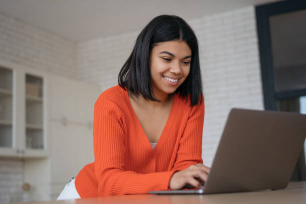 istock African American woman using laptop computer watching training courses, shopping online. Successful copywriter typing on keyboard, looking at laptop screen working freelance project from home 1387809252