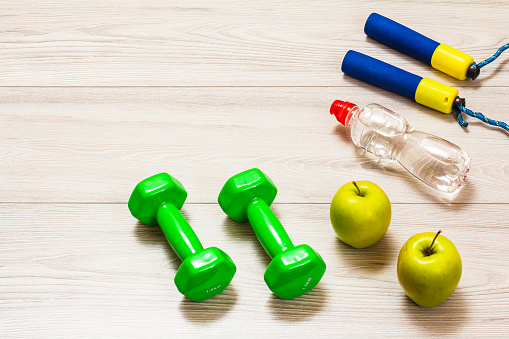 Skipping rope and dumbbells for fitness, a bottle of water and apples in a room or a gym on the gray floor. Top view.