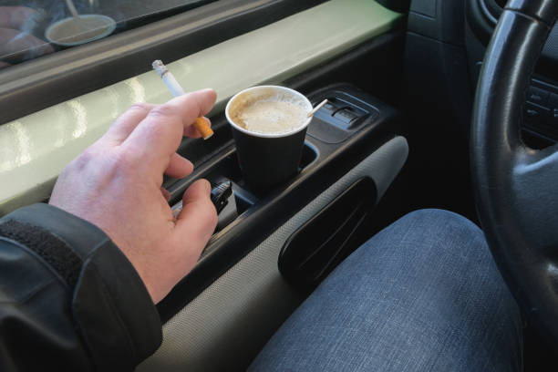 istock Cigarette in hand. Paper disposable coffee cups. Smoking while driving a car while driving. 1387813552
