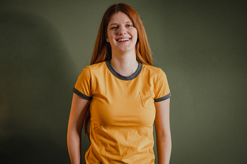 Young woman in a yellow t-shirt, standing in front of the green wall