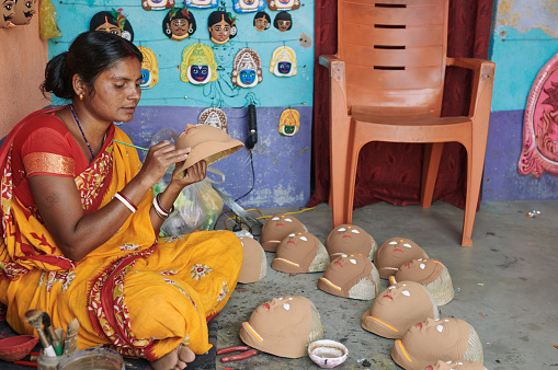 Purulia, West Bengal, 03-13-2022: A rural woman (artisan) applying paint on paper pulp made Chhau (traditional folk dance art from Bengal) masks at Charida village, famous for making Chhau masks.