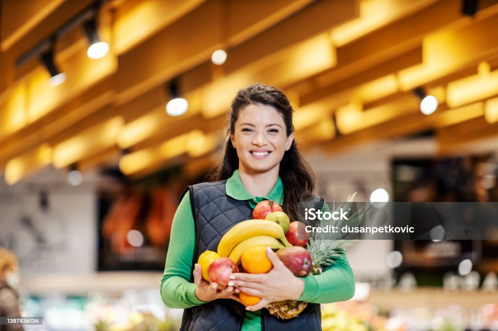 A supermarket employee holding fresh fruits. A saleswoman offering fresh fruits in supermarket. Supermarket Stock Photo
