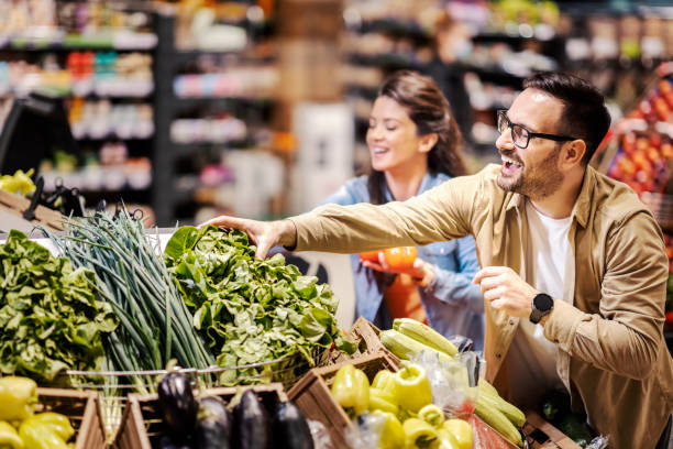 Happy couple buying vegetables at supermarket. Couple choosing and purchasing fresh vegetables at supermarket. consumer confidence photos stock pictures, royalty-free photos & images