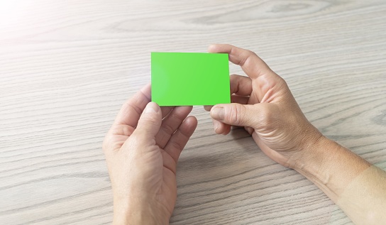 Hands of a woman holding a green screen business card without logos