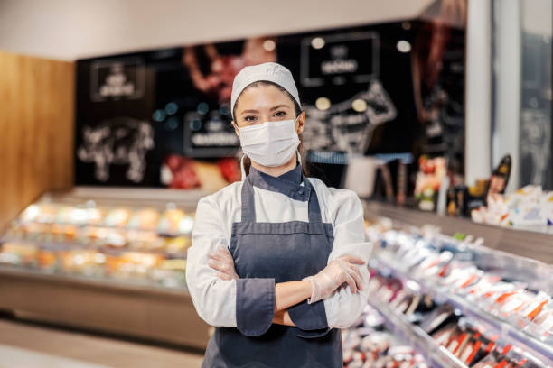 Portrait of a female butcher at supermarket during corona virus. Portrait of a proud meat department worker during covid 19. refrigerated section supermarket photos stock pictures, royalty-free photos & images