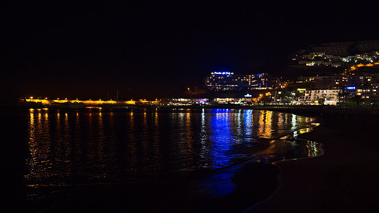 Puerto Rico, Gran Canaria, Spain - 12-29-2021: View of holiday resort Puerto Rico, southern Gran Canaria, Spain at night with illuminated hotel buildings reflected in the water of the Atlantic Ocean.