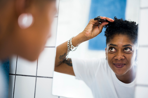 Front view reflection of woman combing curly short hair looking in mirror in bathroom