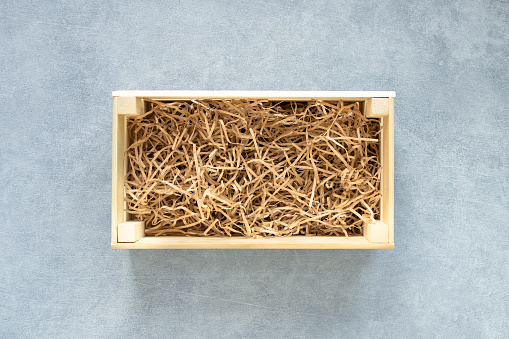 Top view of wooden box for eco gift filled with decorative shredded white paper on gray background.