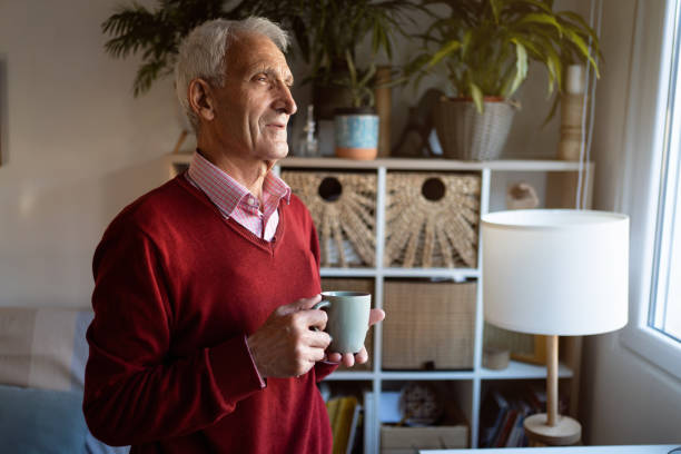 istock Pensive Caucasian senior man, looking through the window while holding cup of coffee 1387836269